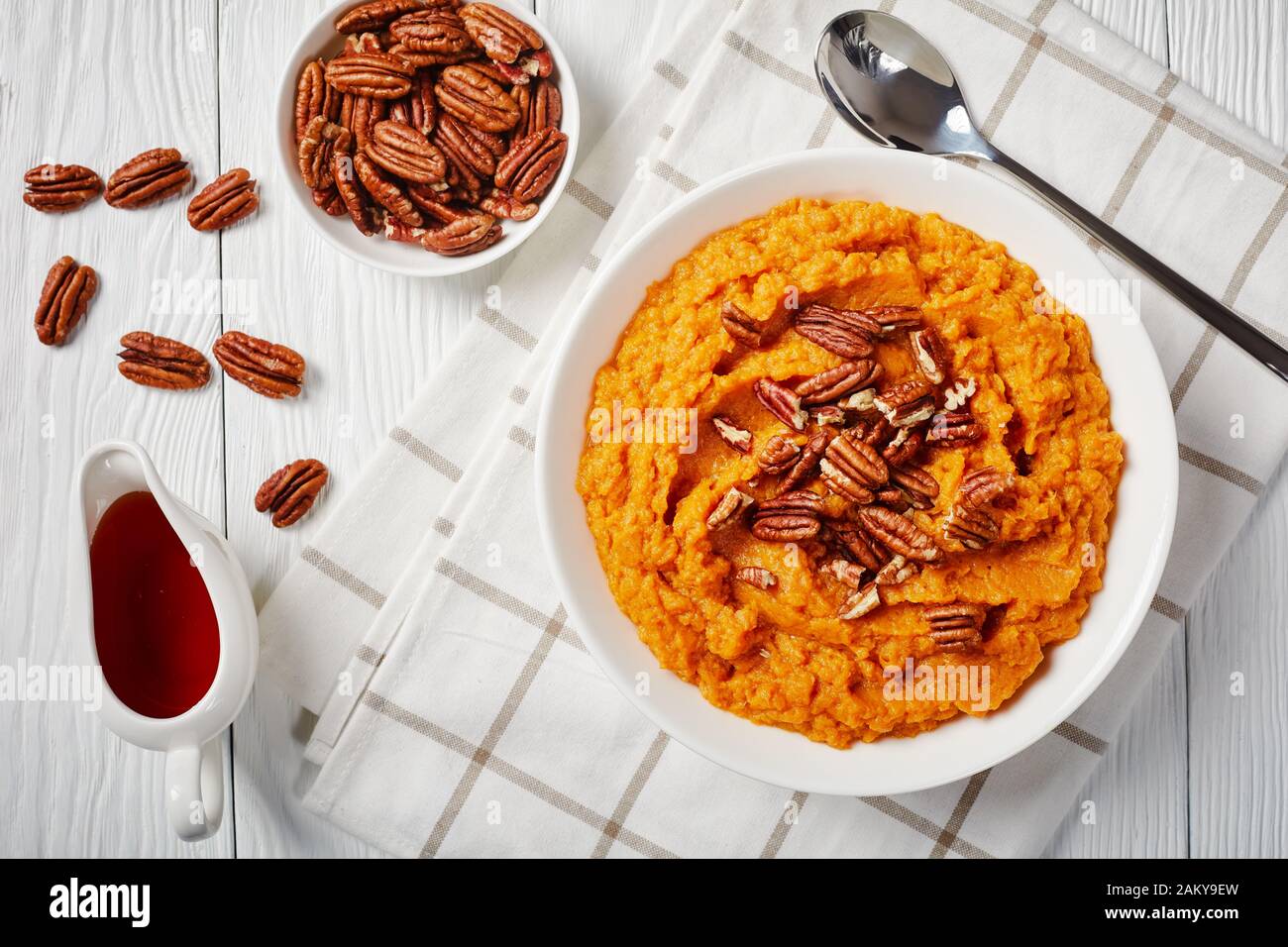 Nahaufnahme köstlicher Kartoffelpüree mit Pekannüssen in einer Schüssel. Ahorn-Sirup in einem weißen Sauceboot auf einem Holztisch, horizontaler Blick von A Stockfoto