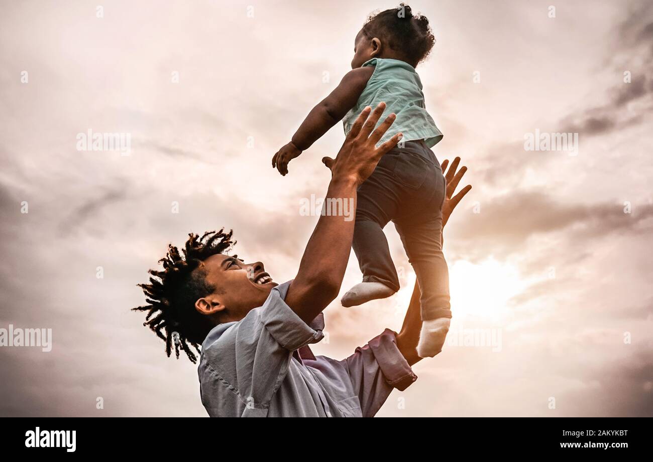 Glücklicher Vater, der mit seiner Tochter bei Sonnenuntergang spielt - die Familie Afro hat Spaß im Freien - Konzept von Kind, Glück und Elternschaft Stockfoto