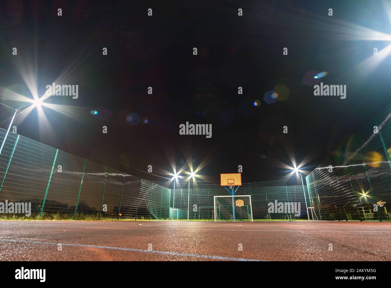 Im freien Mini Fußball- und Basketballplatz mit Ball Gate und Korb mit hoher Schutzzaun hell mit Spotlight Lampen beleuchtet umgeben Stockfoto