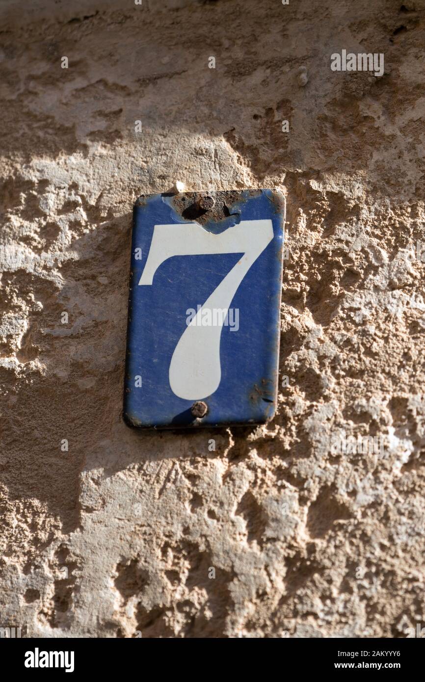 Weiße Nummer Sieben Hausnummer auf einer blauen Metallplatte an einer Steinmauer Stockfoto