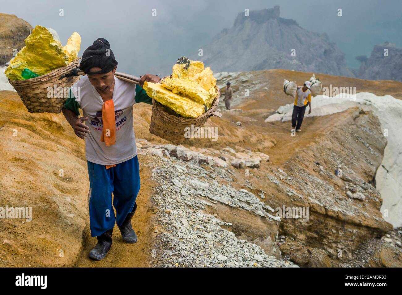 Schwefel-Bergleute, die mit Schwefel beladene Körbe am Kawah Ijen Vulkan in Ostjava, Indonesien tragen. Stockfoto