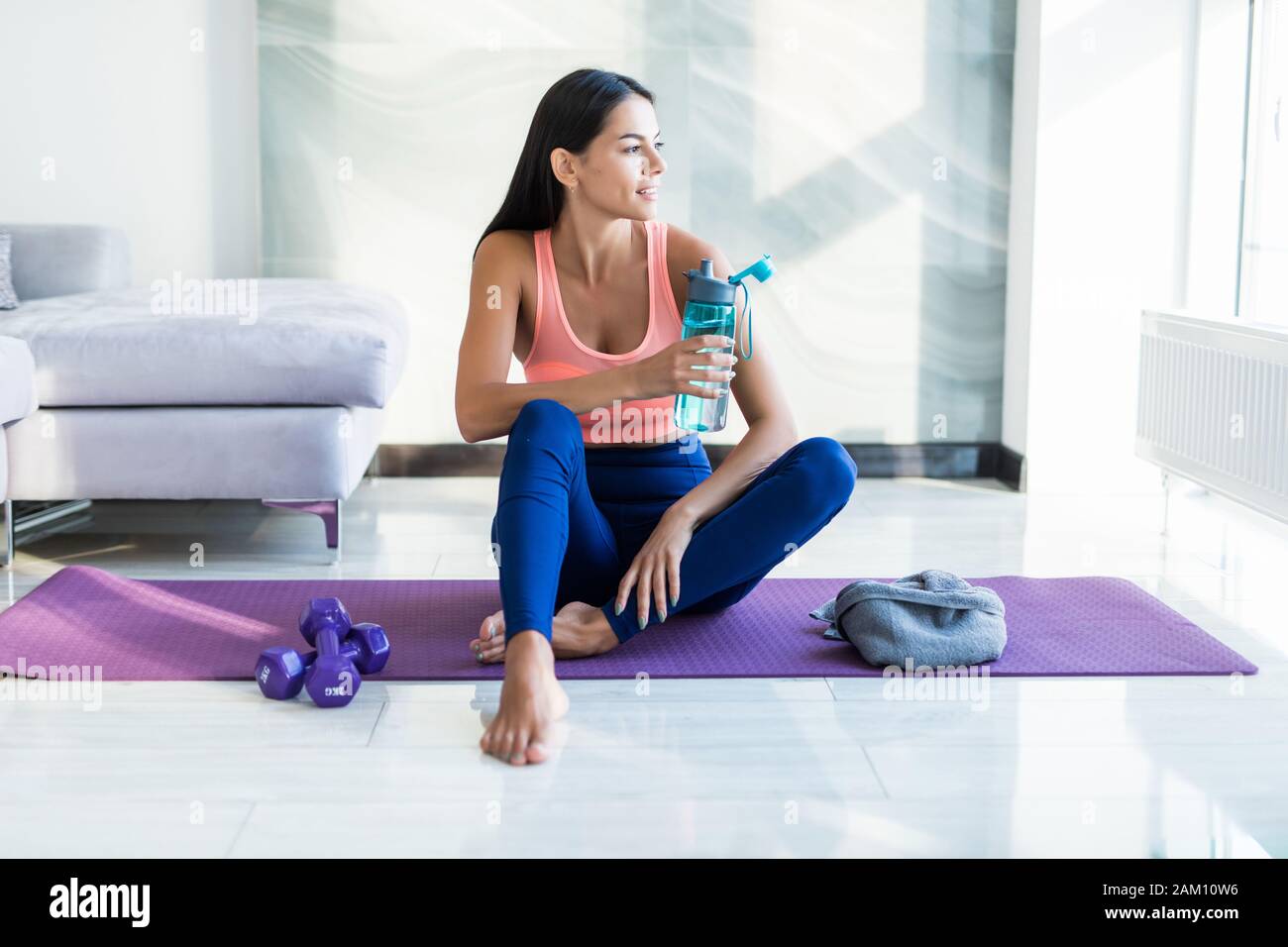 Durstgefühl. Müde Mädchen in Sportbekleidung Trinkwasser während der Sitzung auf die Gymnastikmatte Stockfoto