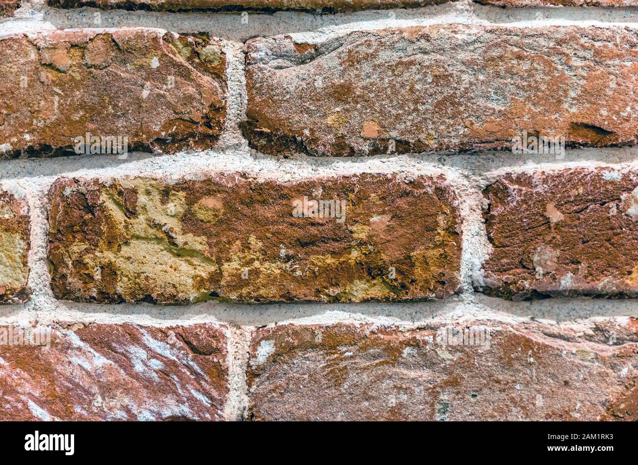 Ein Bruchstück einer Ziegelmauer aus altem, haltbaren Backstein aus rotem gebranntem Ton mit rauer Textur, von Hand gefaltet und mit Zementmörtel mit zementiert Stockfoto
