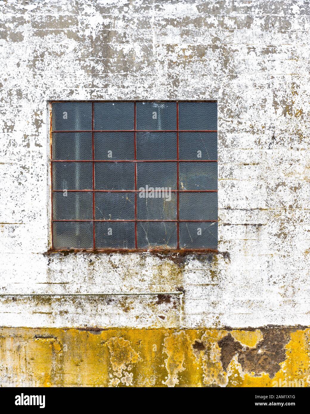 Staubiges Fenster mit einem rostigen Metallschutzgitter in der Wand eines alten verlassenen Betongebäudes mit einer bemalten Wand mit Peeling-Lack und Schimmel Stockfoto