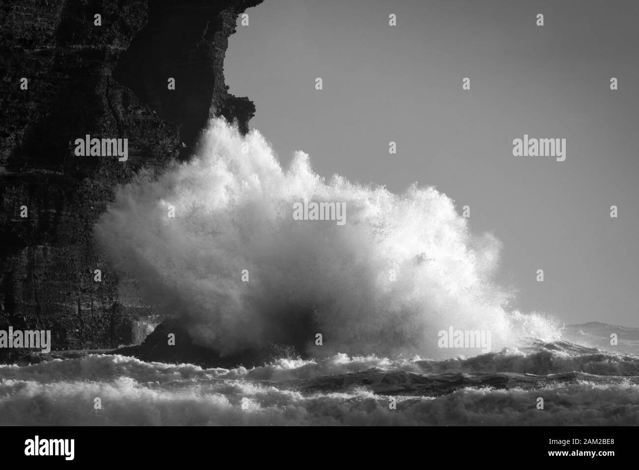 Schwarz-Weiß-Bild von großen Wellen, die gegen die Felsen am Piha Strand, Waitakere, Neuseeland krachen Stockfoto