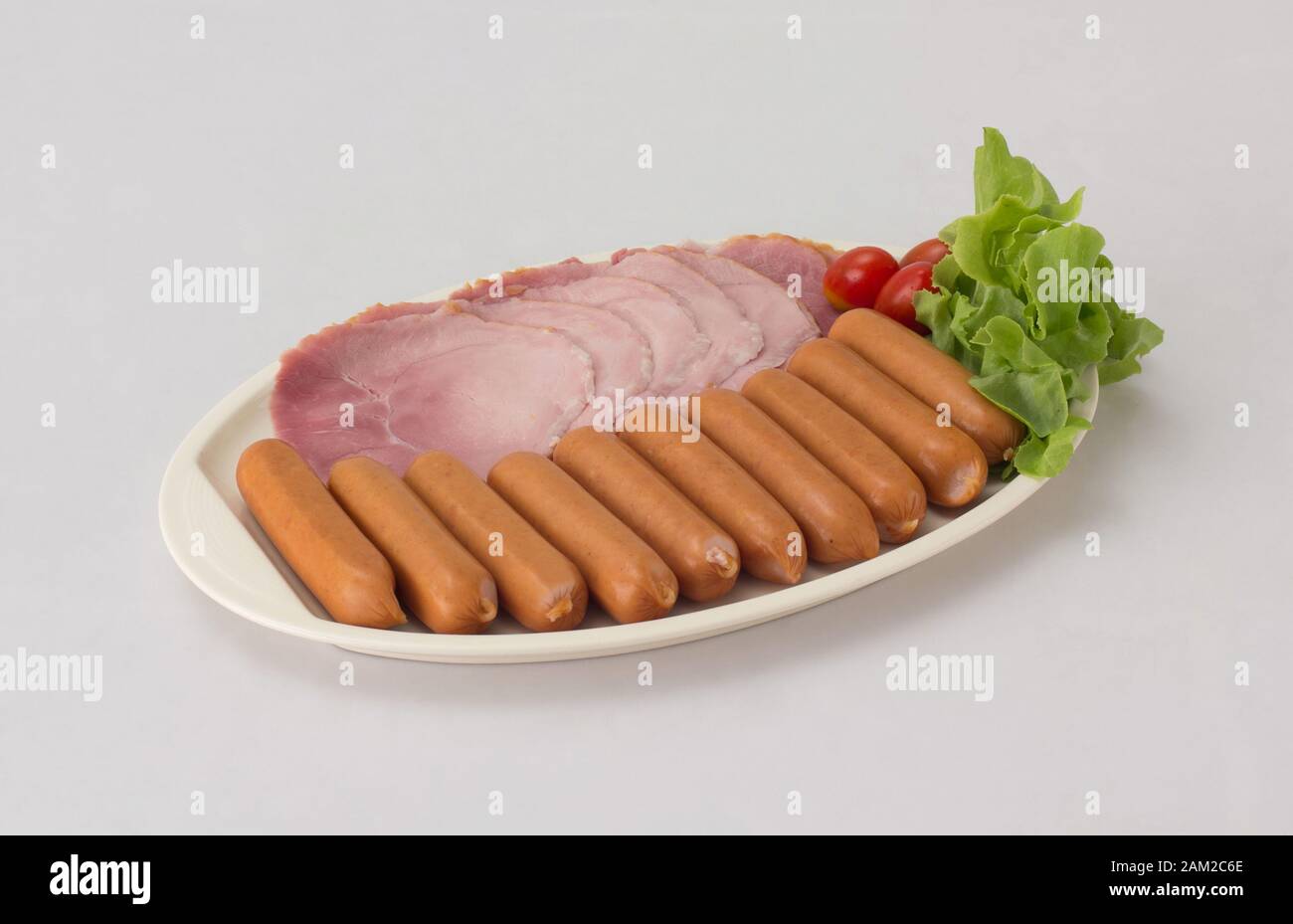 Geräucherte Würstchen und Schinken in Scheiben serviert mit Tomaten und Gemüse auf weißem Gericht isoliert auf weißem Hintergrund Stockfoto