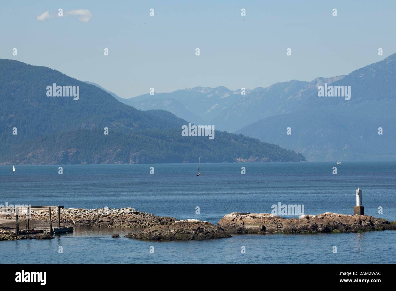 Seamark auf felsiger Halbinsel, segelboot und Bergkette im Hintergrund, Vancouver Island, British Columbia, Kanada Stockfoto