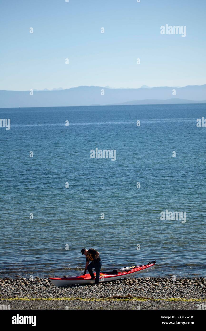 Kajaker und Kajak am Kieselstrand am ruhigen Meer, Vancouver Island, British Columbia, Kanada Stockfoto