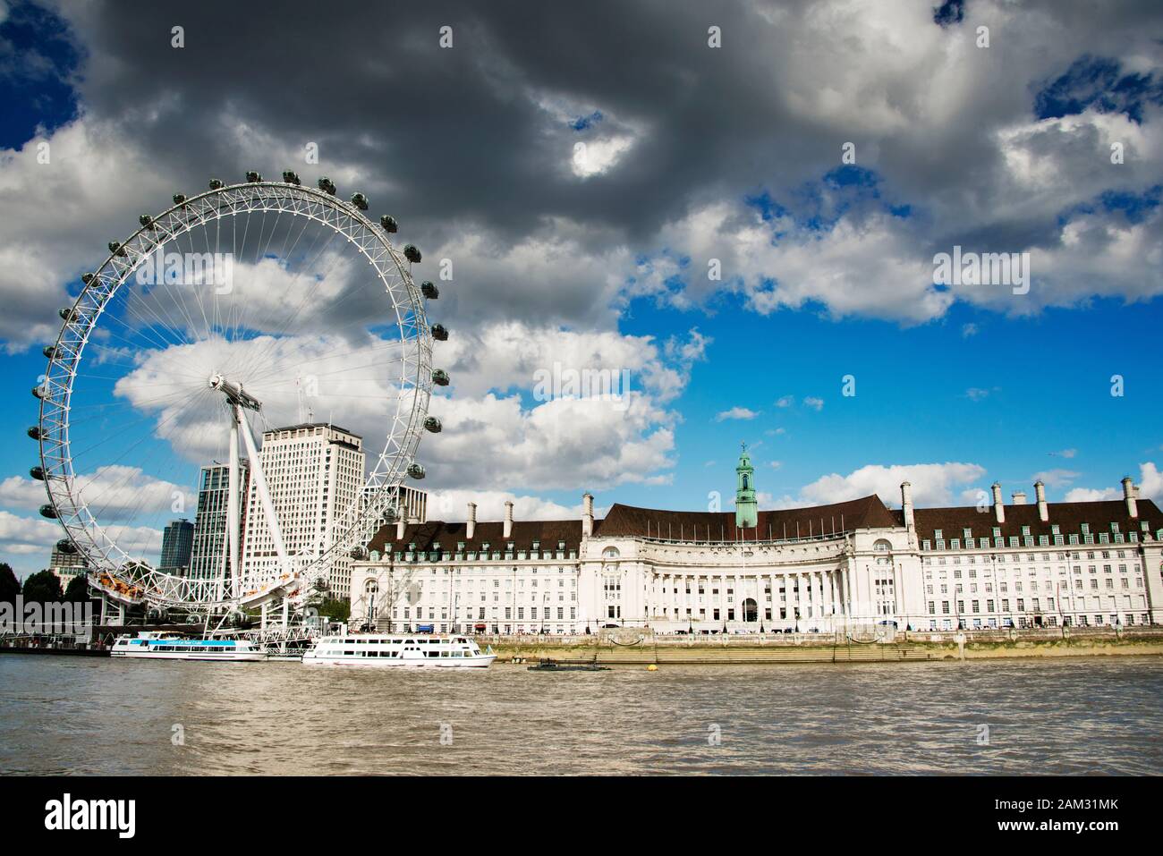 County Hall & London Eye mit Blick auf die Themse und Touristenboote. Mischung aus weißen und dunklen Wolken gegen blauen Himmel Stockfoto