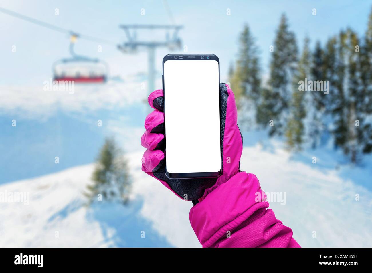 Telefon im Mädchen Hand mit Handschuh auf einem Skilift. Isolierter Bildschirm für Mockup. Skilift, Resort und Pisten im Hintergrund Stockfoto