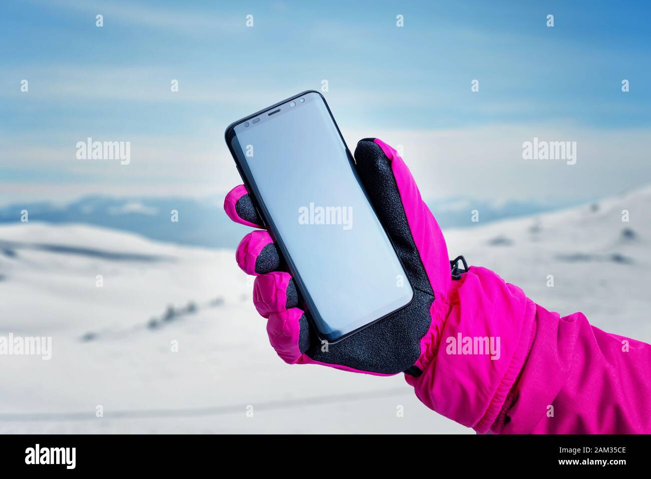 Telefon in der Hand mit Handschuh auf schneebedeckten Bergspitzen. Das Konzept, ein Handy zu nutzen, um einem Wanderweg zu folgen Stockfoto