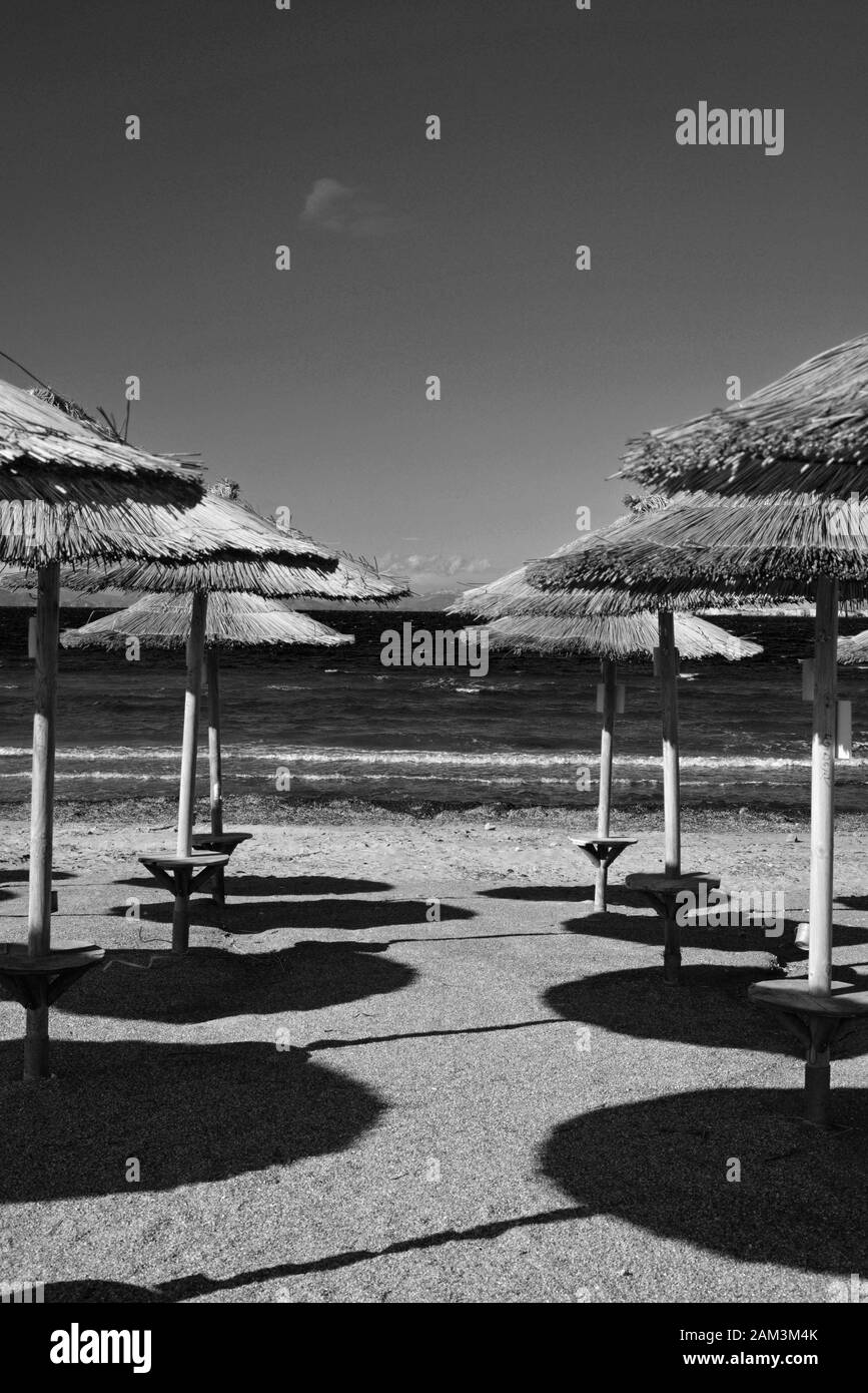 Strohschirme in Reihen, die im Winter an einem leeren Strand in Kavouri, Athen, Schatten auf den Sand werfen. Stockfoto