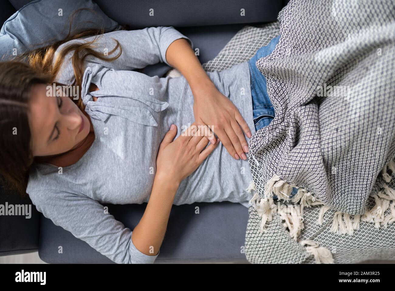 Hohe Betrachtungswinkel und der jungen Frau mit Magenschmerzen auf dem Sofa zu Hause Stockfoto