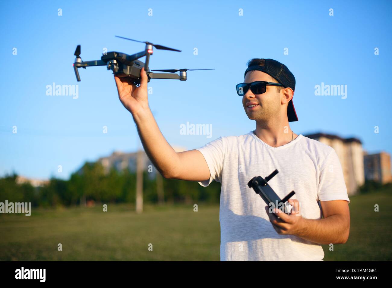 Ein fröhlicher lächelnder Mann hält kleine kompakte Drohne und Fernbedienung in den Händen. Pilot startet Quadcopter aus seiner Hand. Drohne bereit zum Start. Stockfoto