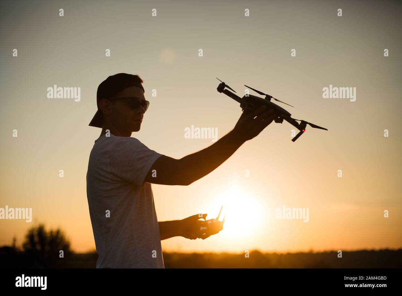 Silhouette eines Mannes, der kleine kompakte Drohne und Fernbedienung in den Händen hält. Pilot startet Quadcopter aus seiner Handfläche bei Sonnenuntergang. Drohne bereit zu Stockfoto