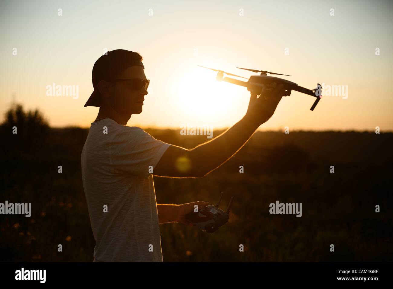 Silhouette eines Mannes, der kleine kompakte Drohne und Fernbedienung in den Händen hält. Pilot startet Quadcopter aus seiner Handfläche bei Sonnenuntergang. Drohne bereit zu Stockfoto