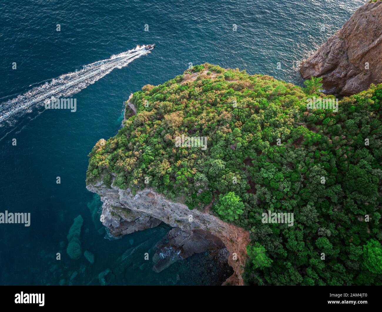 Luftaufnahme von einem steilen Felsen und ein Motorboot. Zerklüftete Küste an der Adria. Klippen mit Blick auf den transparenten Meer. Budva, Montenegro Stockfoto