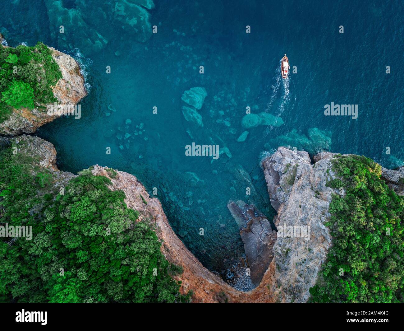 Luftaufnahme von einem steilen Felsen und ein Motorboot. Zerklüftete Küste an der Adria. Klippen mit Blick auf den transparenten Meer. Budva, Montenegro Stockfoto