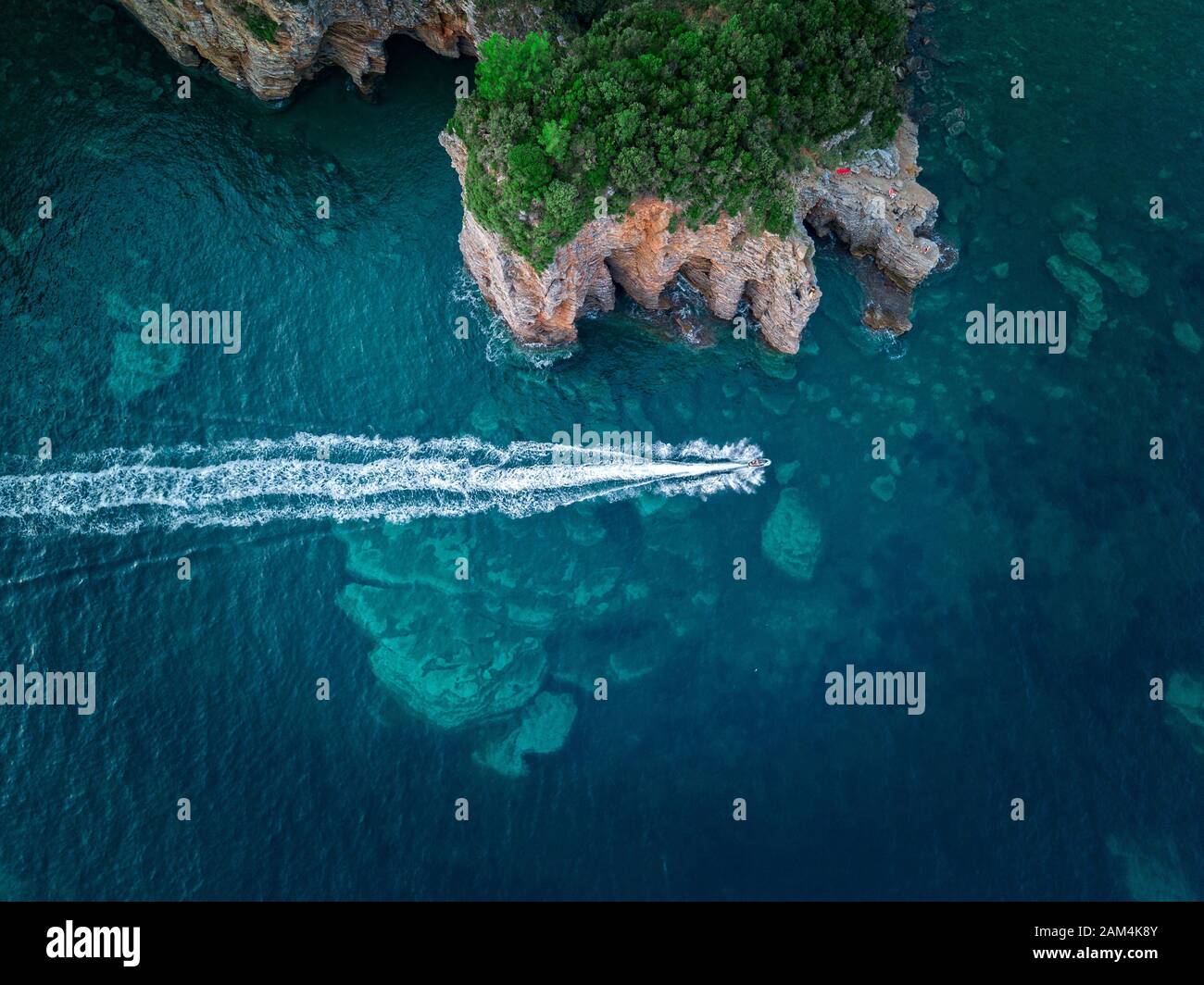 Luftaufnahme von einem steilen Felsen und ein Motorboot. Zerklüftete Küste an der Adria. Klippen mit Blick auf den transparenten Meer. Budva, Montenegro Stockfoto