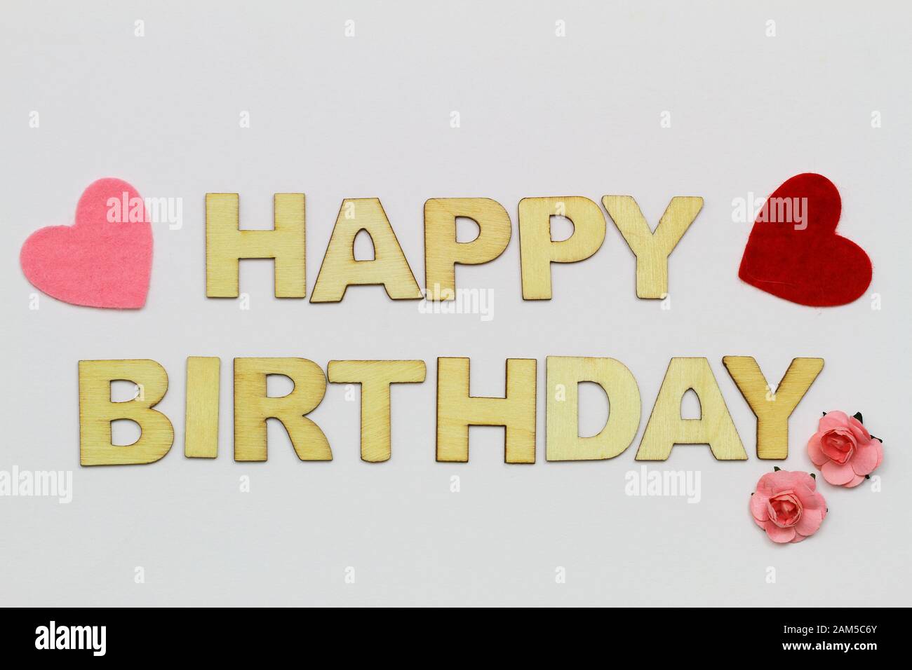Alles gute zum Geburtstag mit Holzbuchstaben auf weißer Oberfläche, Herzen und pinkfarbenen Papierrosen Stockfoto