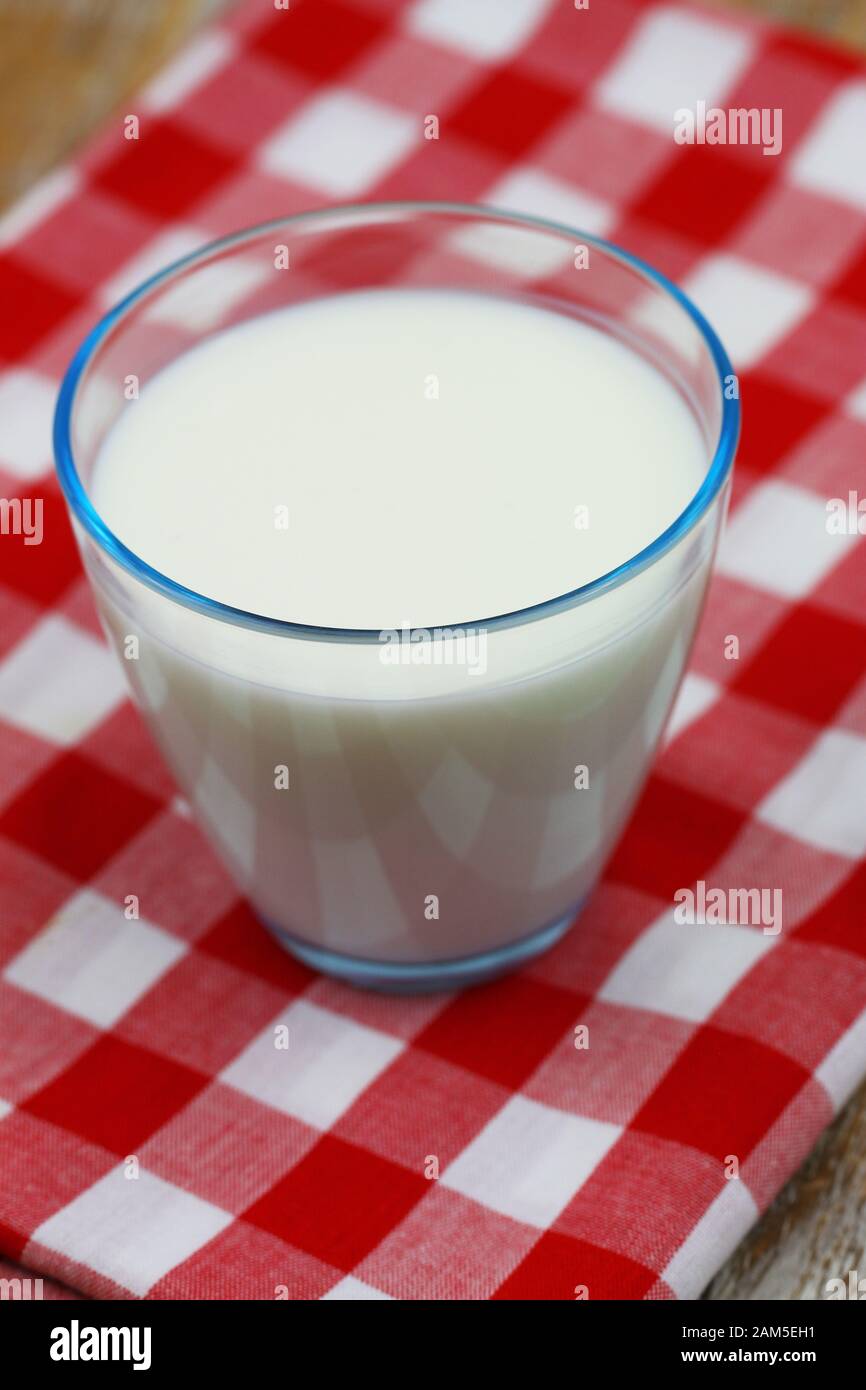 Glas frischer Milch in transparentem Glas auf rotem und weißem kariertem Tuch Stockfoto