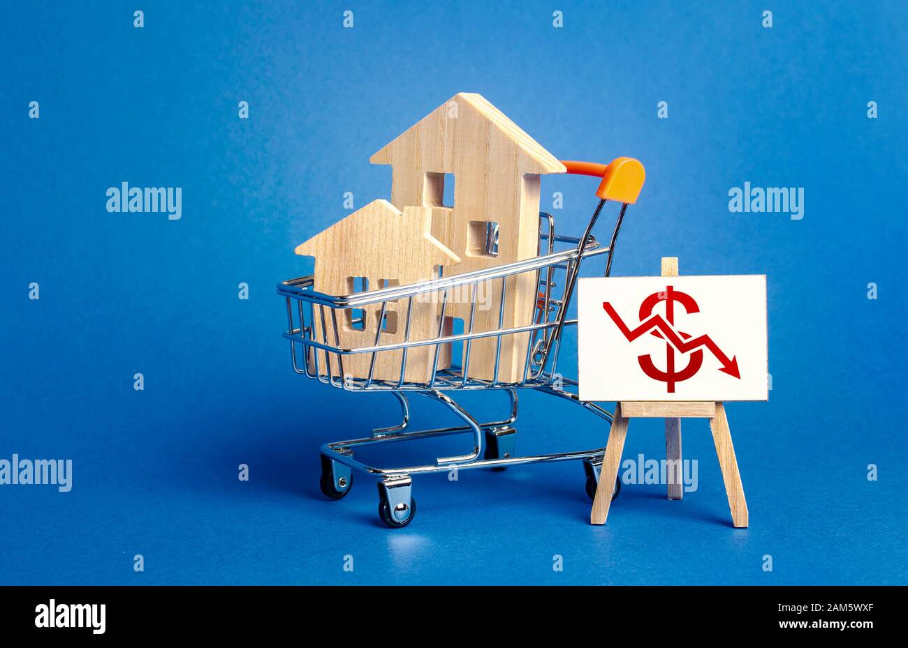 Holzhäuser in einem Einkaufswagen und eine Staffelei mit einem roten Dollarpfeil nach unten. Fall des Immobilienmarktes. Günstige Miete. Geringere Nachfrage, Rezession. L Stockfoto