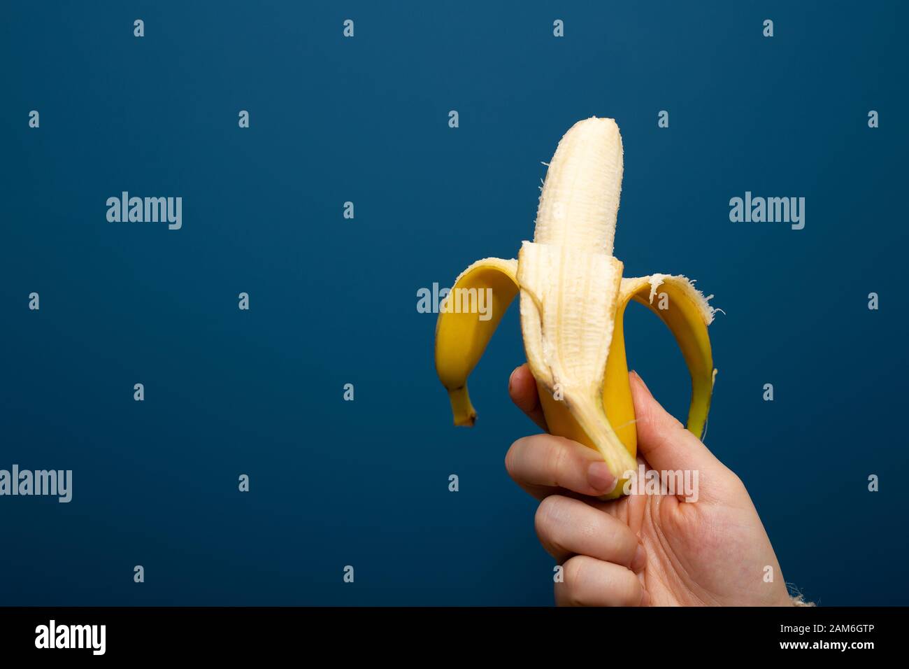 Geschälte gelbe Bananenfrucht nahe blauem Hintergrund in der Hand, gesundes Konzept Stockfoto