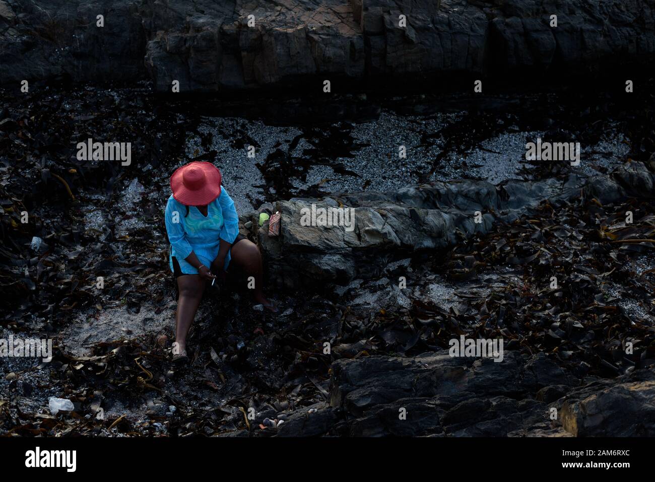 Eine Frau in einem sonnenhut raucht eine Zigarette auf einem Strand in Kapstadt Atlantikküste Vorort von Seapoint in Südafrika Stockfoto