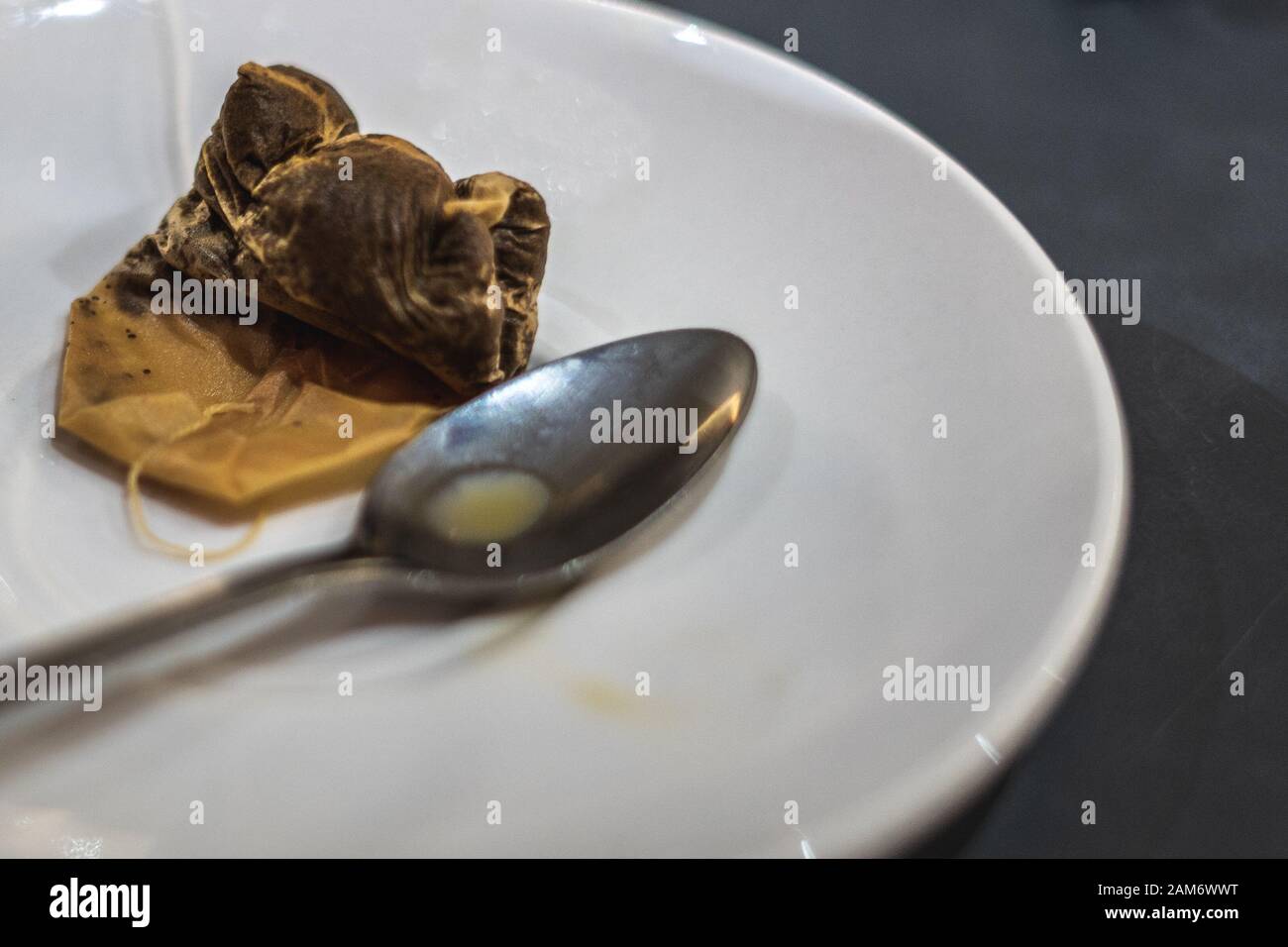 Eine gebrauchte Teetasche auf einer weißen Untertasse neben einem schmutzigen Teelöffel Stockfoto