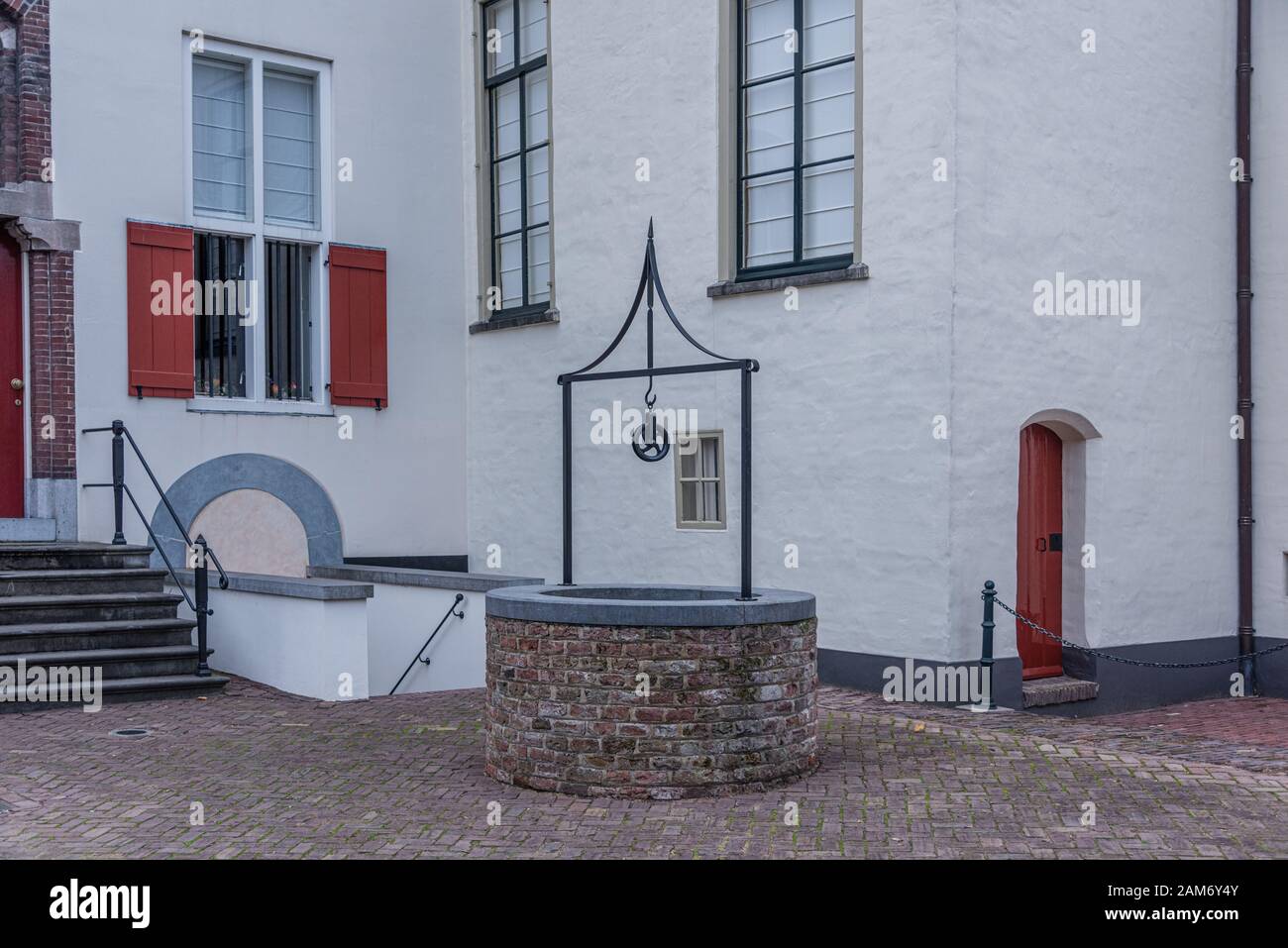 Klassisches Steinwasser in urbaner Umgebung mit einem Kettenzug gegen eine weiße Wand an einer Steinstraße Stockfoto