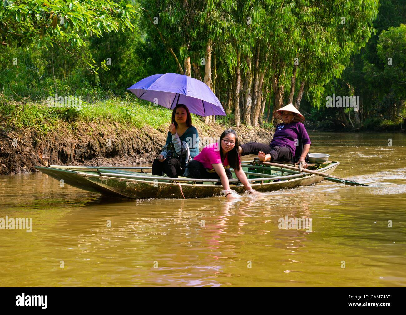 Asiatische Touristen im Sampan, die von der einheimischen Frau mit konischem Hutrudern mit Füßen, Tam Coc, Ninh Binh, Vietnam, Asien, gerochen werden Stockfoto