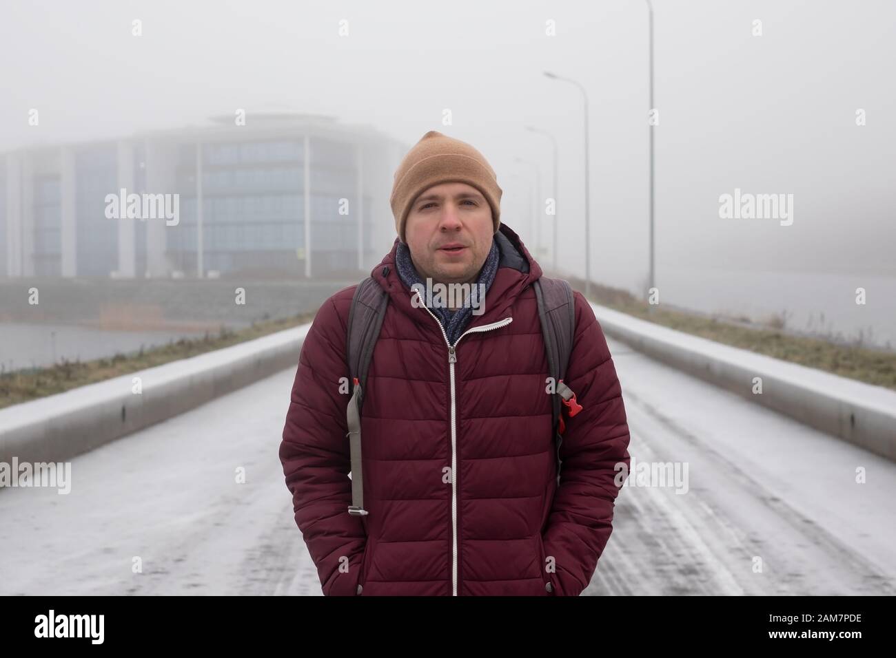 Junger trauriger kaukasischer Mann in warmem Hut und Mantel, der im Winter allein im Freien steht Stockfoto