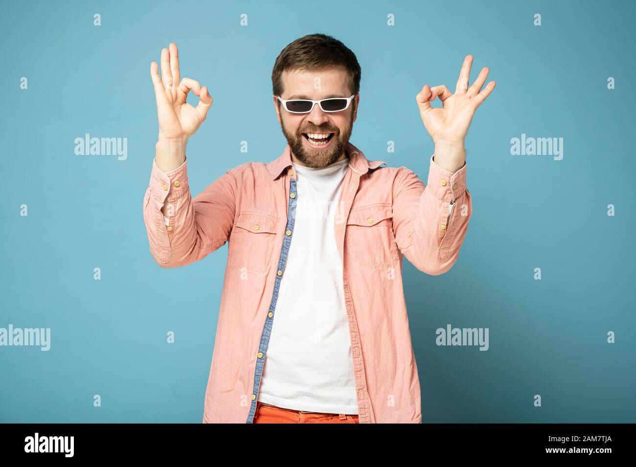 Ein glücklicher bärtiger Mann in der Sonnenbrille zeigt eine gute Geste und lächelt breit. Stockfoto