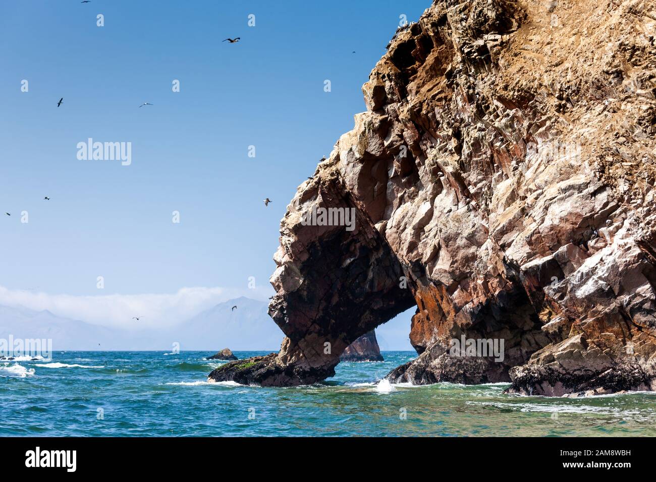 Ein Felsen mit einer Grotte mit Blick auf das Meer, Möwen fliegen herum, Berge, Ballestas-Inseln sind in der Ferne zu sehen, Paracas Rum, Peru, Latin Stockfoto