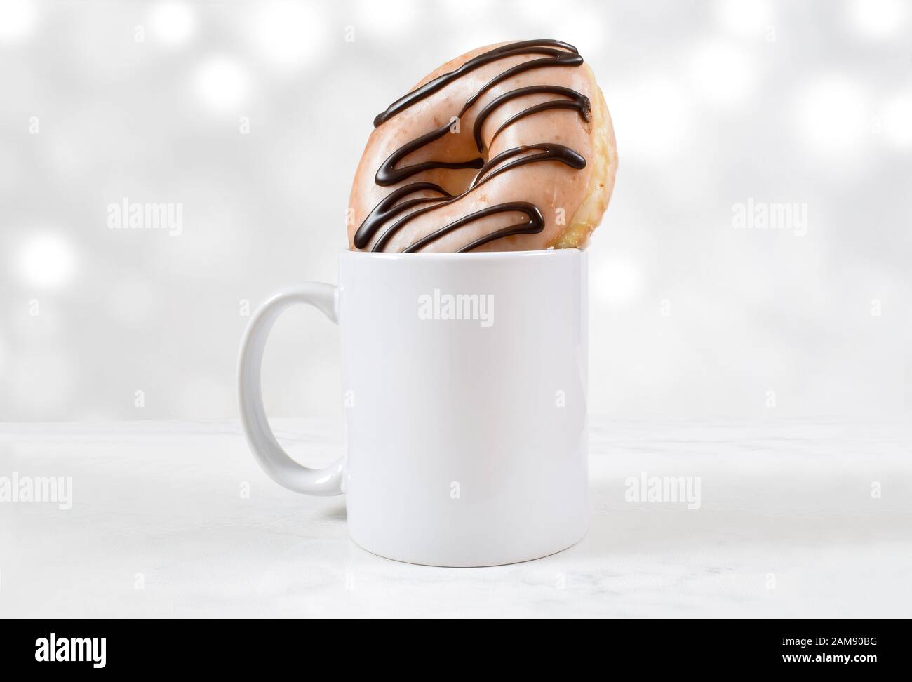 Ein Dönut aus glasiertem und schokoladenhaltigem Dönut sitzt freudig in einem leeren weißen 11 oz Kaffeebecher. Weiße Bokeh-Lichter leuchten im minimalistischen Mockup. Rea Stockfoto