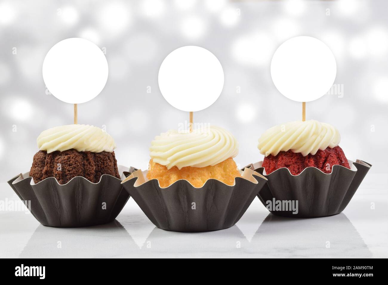 Ein verführerisches Cupcake-Topp mit drei leckeren Gourmet-Cupcakes auf weißem Marmorhintergrund. Fügen Sie Ihren eigenen Entwurf zu den Kupentürenoberhäuschen hinzu. Stockfoto