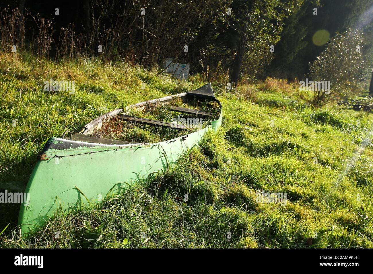 Das alte Kanu liegt auf der Wiese in Flussnähe und ist verlassen, von Gras überwuchert und nutzlos. Stockfoto