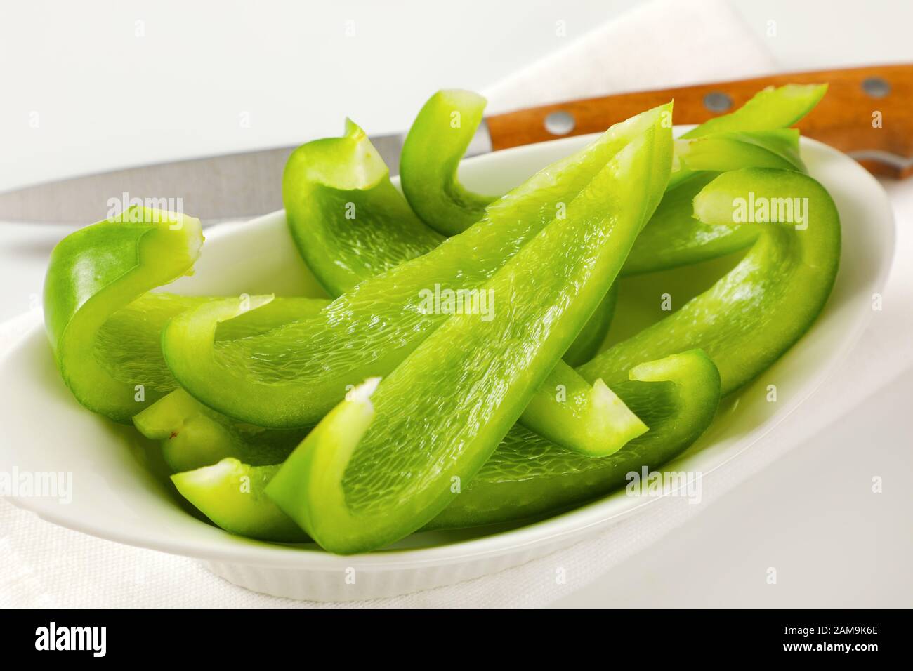 Grüner Paprika in weißer Schüssel und Küchenmesser daneben geschnitten Stockfoto