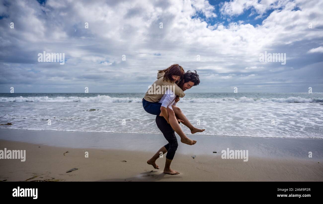 Asiatische Mädchen reiten Huckepack auf einem Asiaten bei Malibu Beach, Kalifornien, USA Stockfoto