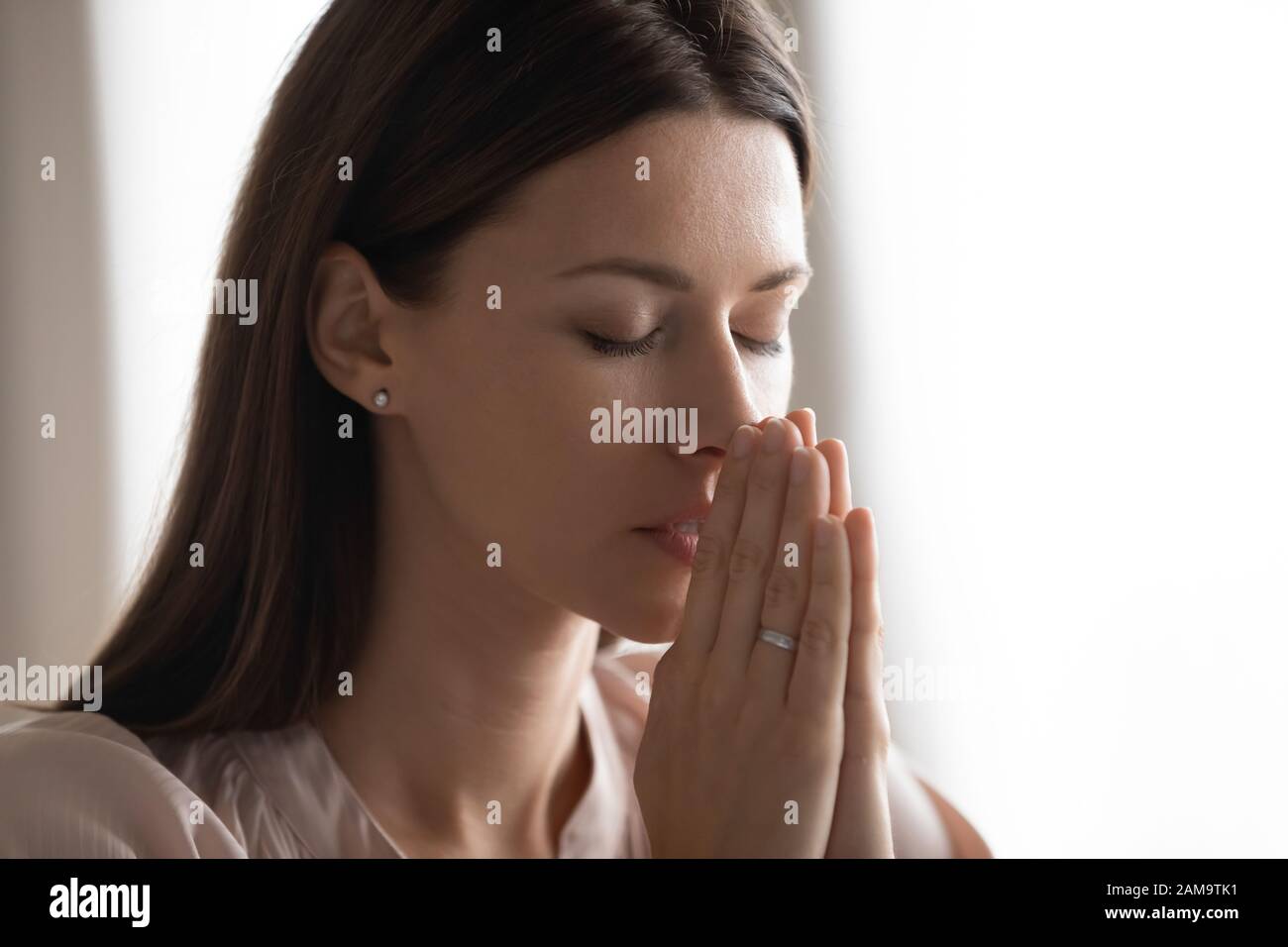 Religiöse junge Frau hält die Hände, die zu Hause beten Stockfoto