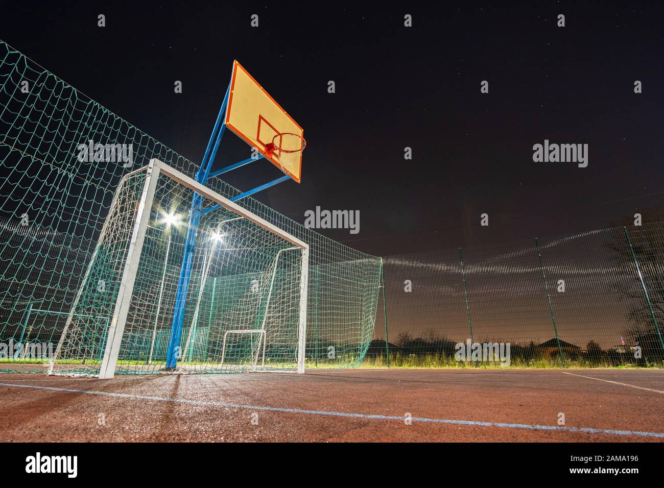 Im freien Mini Fußball- und Basketballplatz mit Ball Gate und Korb mit hoher Schutzzaun hell mit Spotlight Lampen beleuchtet umgeben Stockfoto