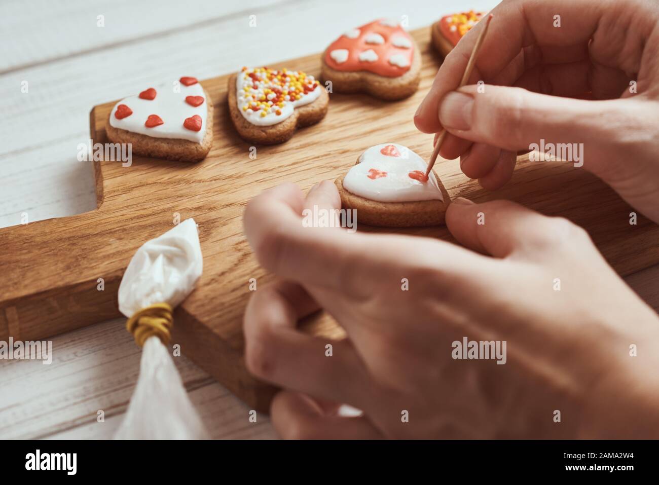 Dekoration Lebkuchen Kekse mit Zuckerguss. Frau Hände Cookies in Form von Herzen schmücken, Nahaufnahme Stockfoto