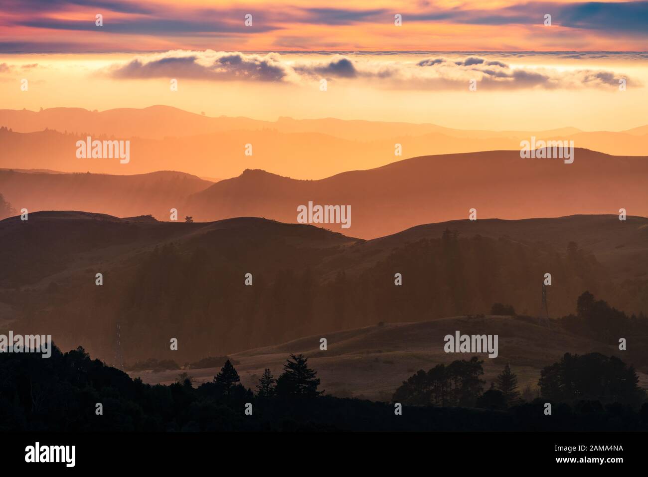 Blick auf den Sonnenuntergang über geschichteten Hügeln und Tälern in den Bergen von Santa Cruz; Wolken über dem Himmel und dem Pazifischen Ozean, die im Hintergrund zu sehen sind; San Francis Stockfoto