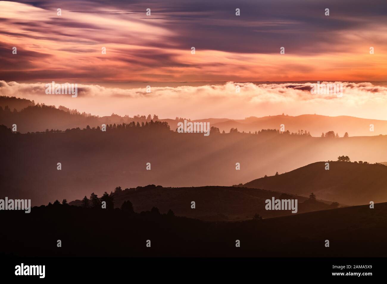 Blick auf den Sonnenuntergang über geschichteten Hügeln und Tälern in den Bergen von Santa Cruz, Wolken über dem Himmel und dem Pazifischen Ozean, San Francisco Bay Area, Kalifornien Stockfoto