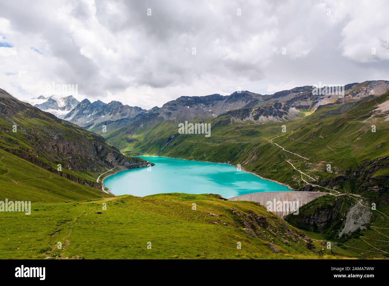 Blick auf den Stausee Lac de Moiry und den Betondamm, umgeben von grünen Almen hoch oben in den Penninischen Alpen an trübem Tag im Sommer. Grime Stockfoto