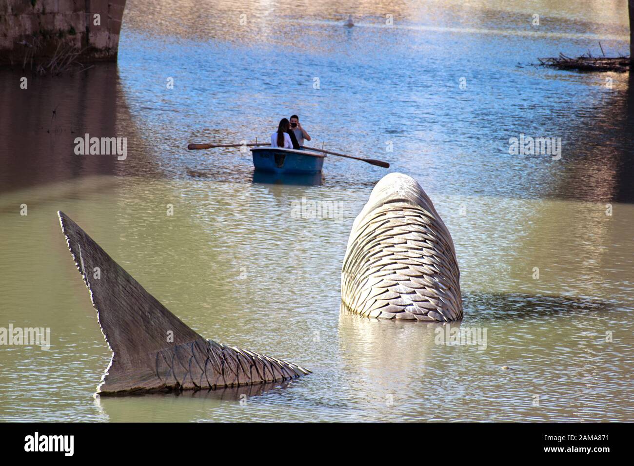 Murcia, Murcia, Spanien. Januar 2020. Riesige Fischskulptur im Fluss Segura gegen Menschen, die auf dem Boot rasten. Stockfoto