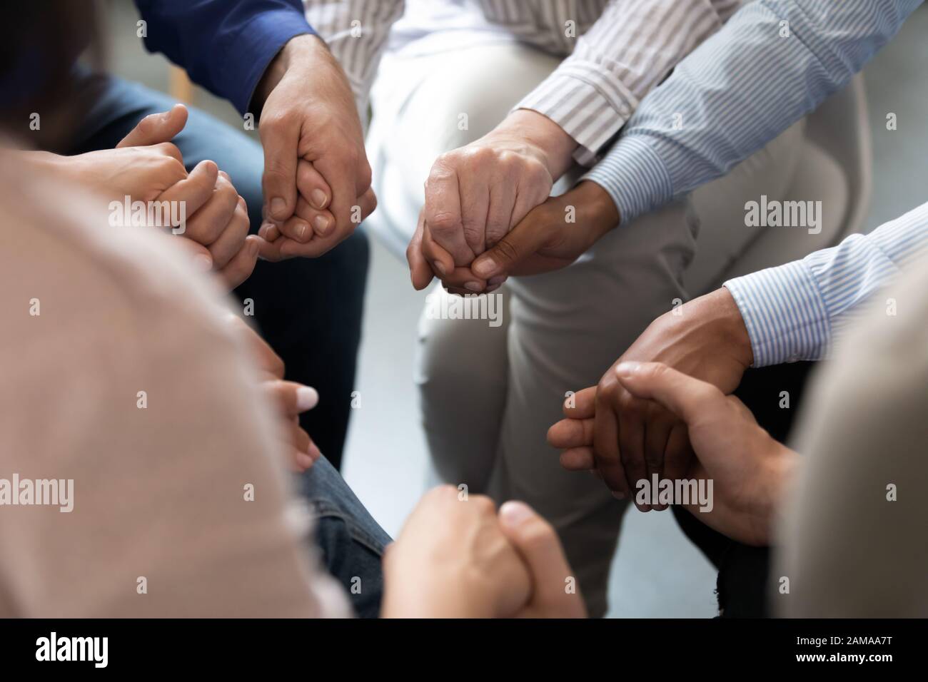 Menschen, die im Kreis sitzen und die Hände während der Gruppentherapiesitzung halten Stockfoto