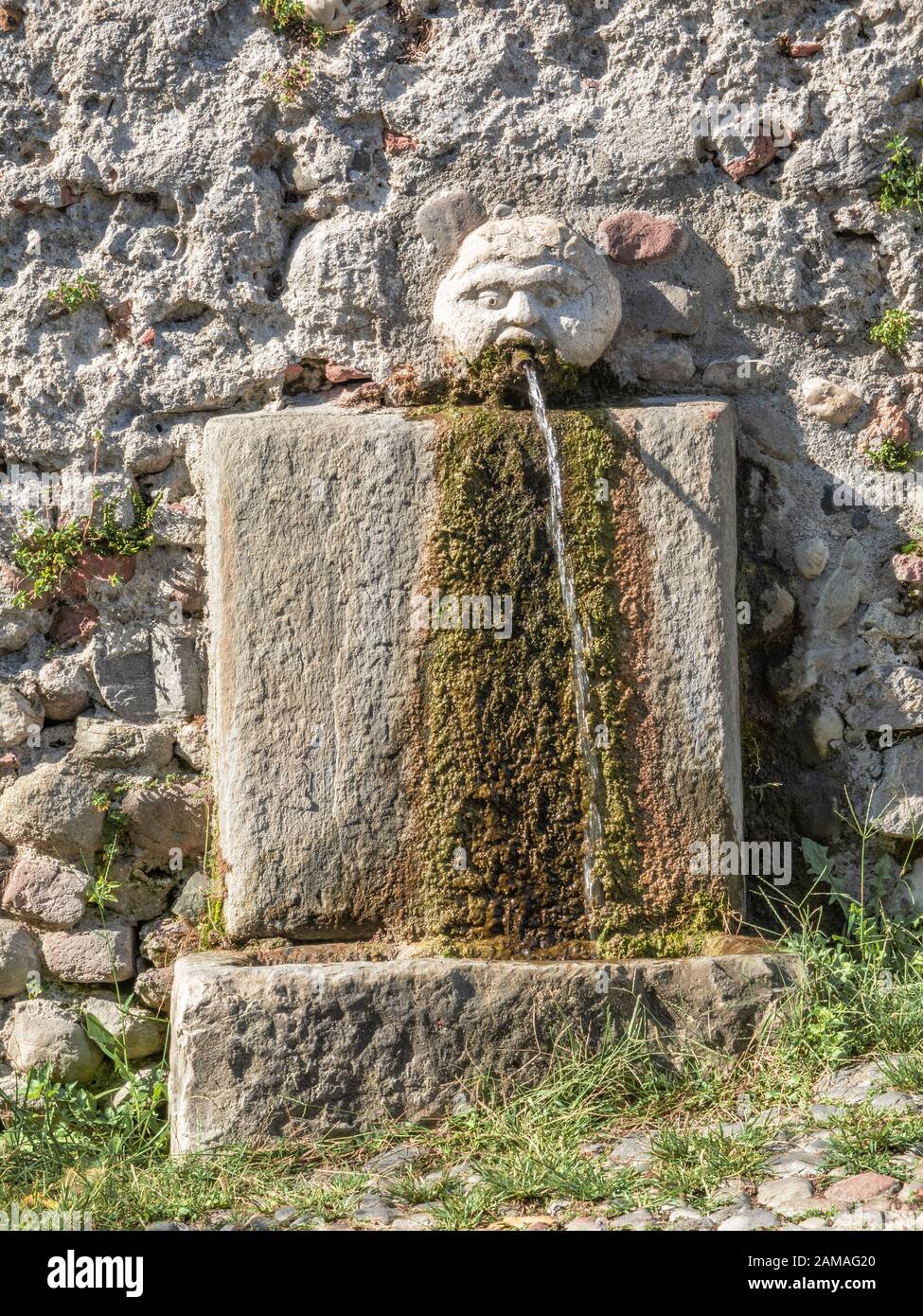Jahrhundert alter Steinbrunnen mit Wasser, das aus dem Mund eines menschlichen Gesichts fließt Stockfoto