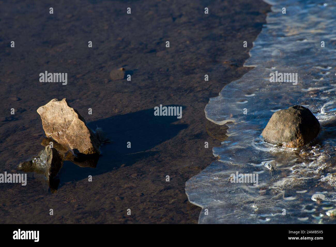 Klassisches und minimales Bild von Wasser und Eis aus Stein, das in Nahaufnahme gefangen ist und wunderschönes Licht mit der Sonne, die sowohl Steine als auch Eis hervorhebt Stockfoto