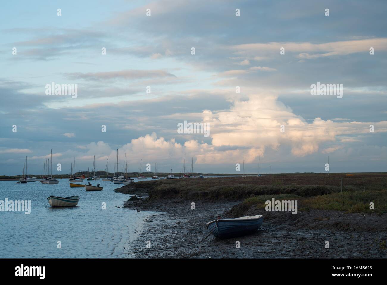 Am frühen Abend im Brancaster Staithes in North Norfolk mit Blick auf das Meer mit Jachten und einem Hintergrund von sonnigen Wolken und hellblauem Himmel Stockfoto